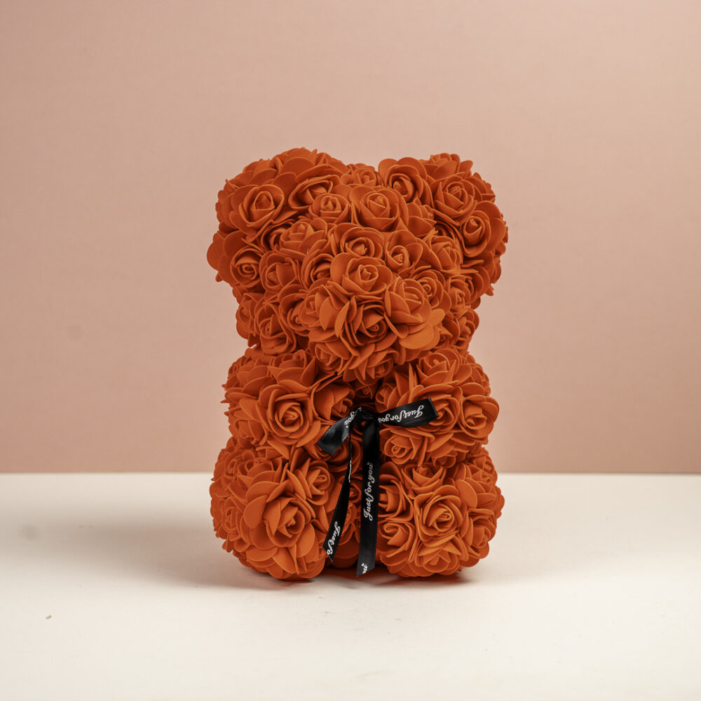 un ours en forme de sculpture, composé de petites roses de couleur orange brûlé. L'ours est décoré d'un ruban noir avec l'inscription "Just for you" en blanc, noué autour de son cou. Le fond violet foncé crée un contraste saisissant avec la couleur chaude de l'ours.